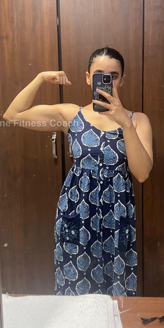 Mrunmayee after: a mirror selfie in a blue printed dress, flexing one arm, face covered by the phone.
